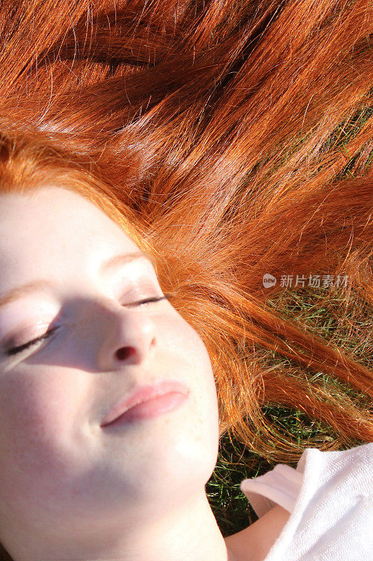 14 / 15岁的红发少女，皮肤苍白，雀斑躺在草地上，眼睛闭着，头发散布在她的头上